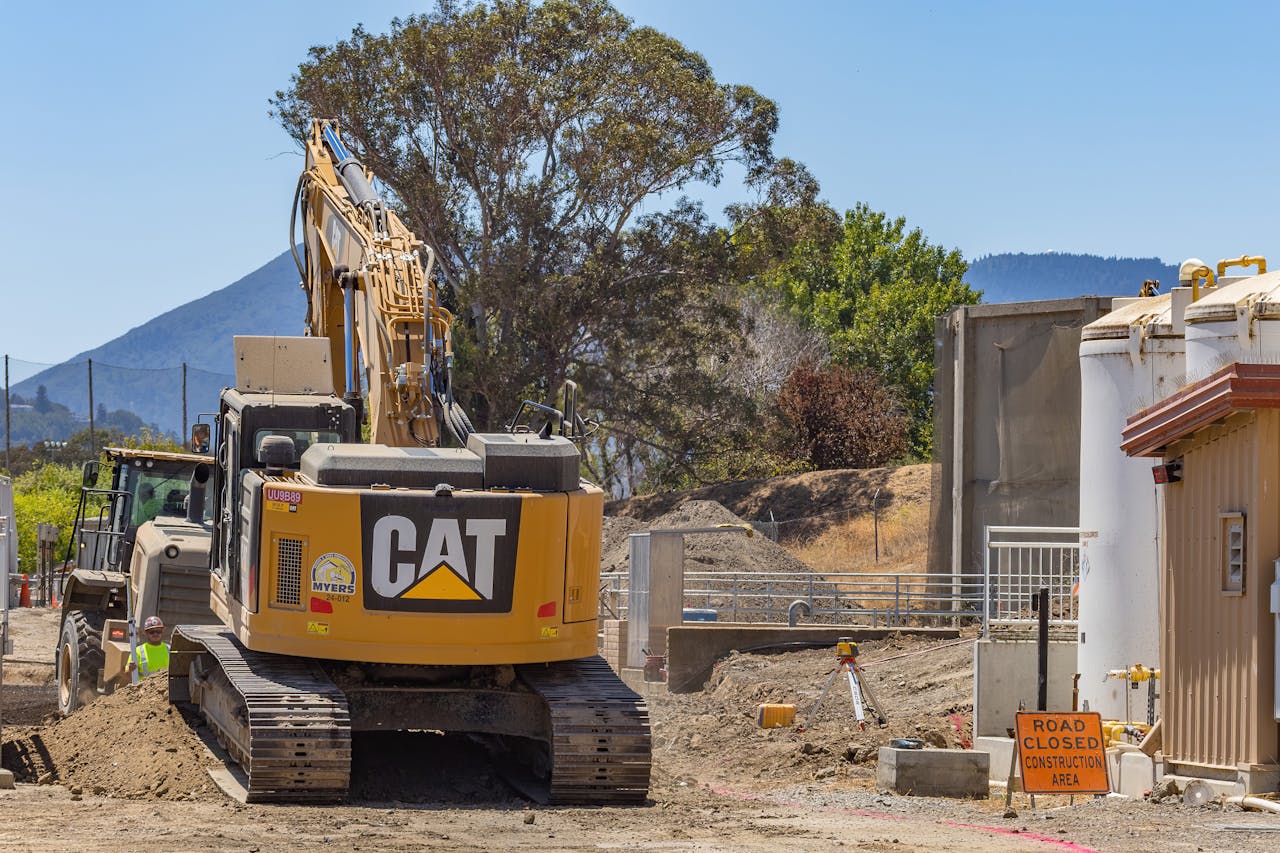 Excavator at a construction site with a road closed sign and mountainous backdrop.