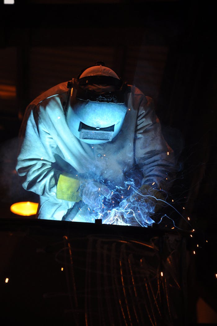 A skilled welder working in a dark workshop with blue sparks flying, showcasing metalworking expertise.