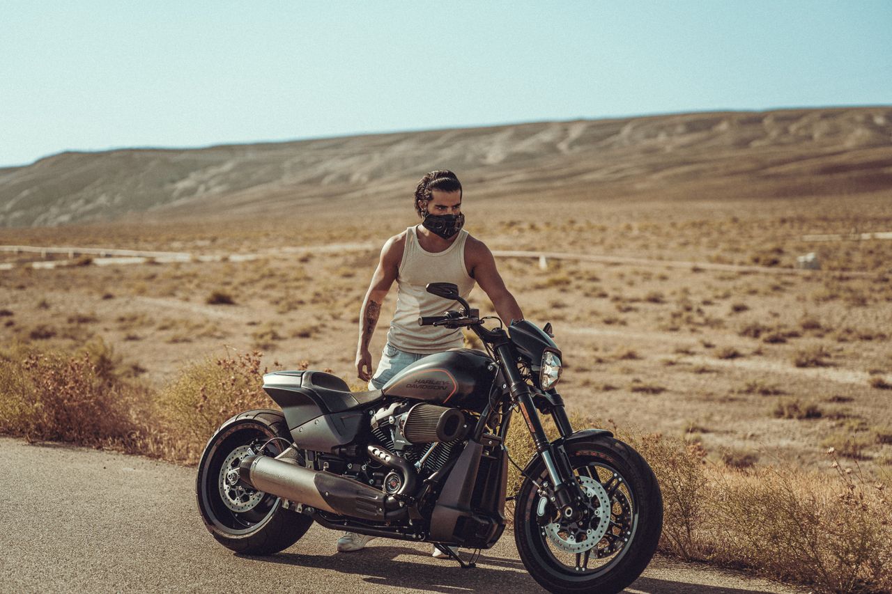 who-we-are A man with a face mask stands by his motorcycle in the barren desert landscape of Baku.